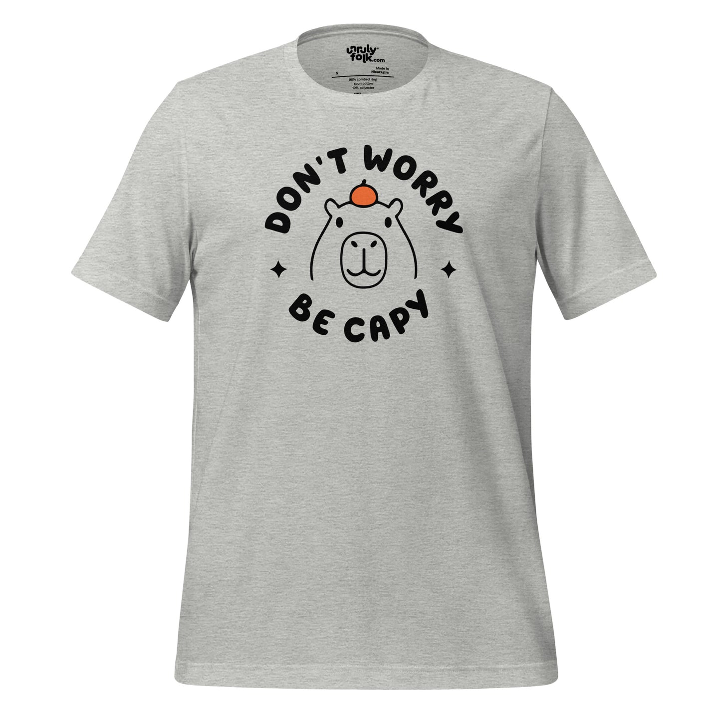 The image is of an athletic heather t-shirt with a slogan that says "Don't Worry Be Capy". It has a line drawing of a capybara with an orange on its head. From the Unruly Folk brand.